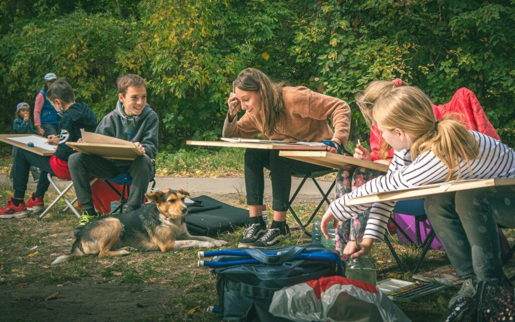 Children learning to draw outdoors with a dog nearby