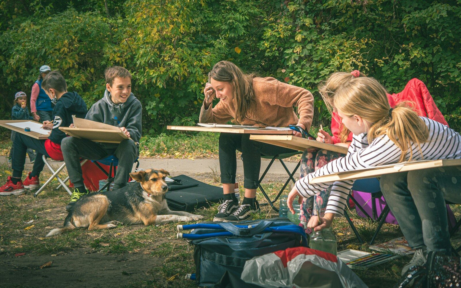 Children learning to draw outdoors with a dog nearby